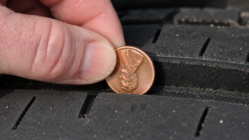 Close-up of fingers inserting a penny head-first into the main circumferential groove of a car tire