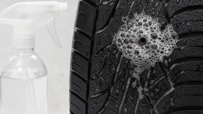 Spray bottle applying soapy water to a tire, with visible bubbles forming at the leak point on the tread